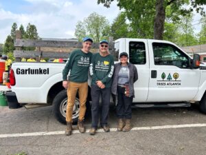 Volunteers John McFarland and Tony Fiore stand with Forest Restoration Coordinator Vicki Mendez in front of a white truck with Trees Atlanta's logo.